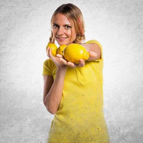 Schöne blonde Frau hält Zitronen auf strukturiertem Hintergrund — Stockfoto
