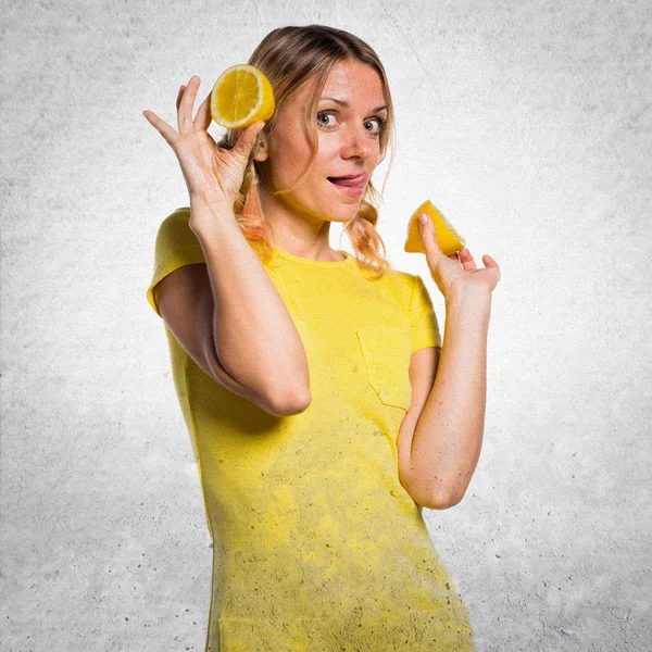 Beautiful blonde woman holding lemons on textured background — Stock Photo, Image