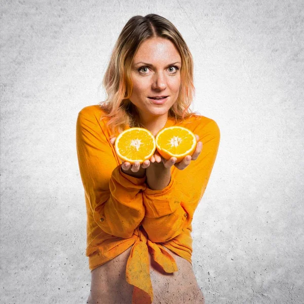 Krásná blondýna žena držící pomeranče na podklad s texturou — Stock fotografie