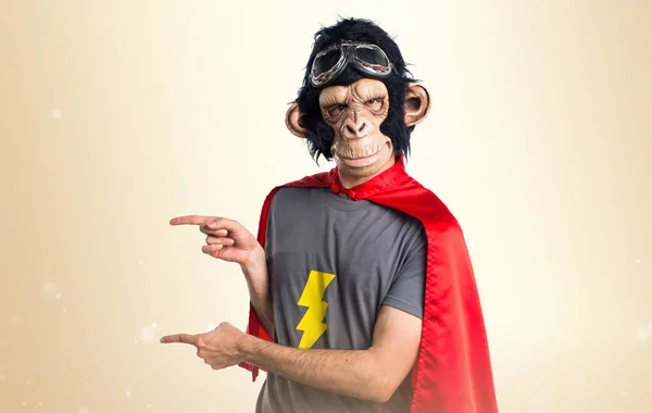 Superhero monkey man pointing to the lateral on ocher background