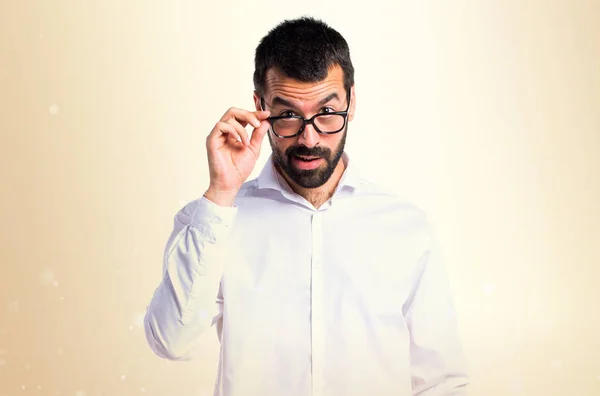 Pohledný muž s brýlemi ukazuje něco na pozadí okrové — Stock fotografie