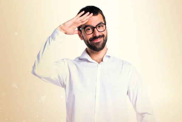 Pohledný muž s brýlemi zdravení na okrové pozadí — Stock fotografie