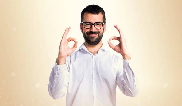 Hombre guapo con gafas haciendo OK signo sobre fondo ocre — Foto de Stock