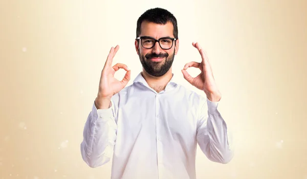 Beau homme avec des lunettes faisant signe OK sur fond ocre — Photo