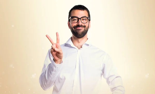 Schöner Mann mit Brille macht Siegergeste auf ockerfarbenem Rücken — Stockfoto