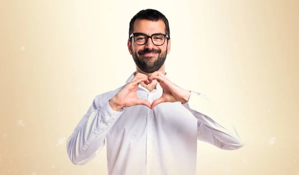 Bell'uomo con gli occhiali che fa un cuore con le mani sull'ocra — Foto Stock