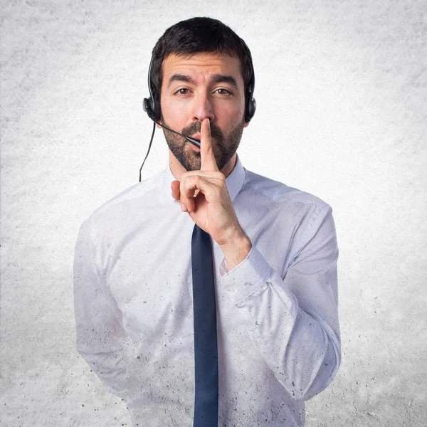 Young man with a headset making silence gesture on textured back — Stock Photo, Image