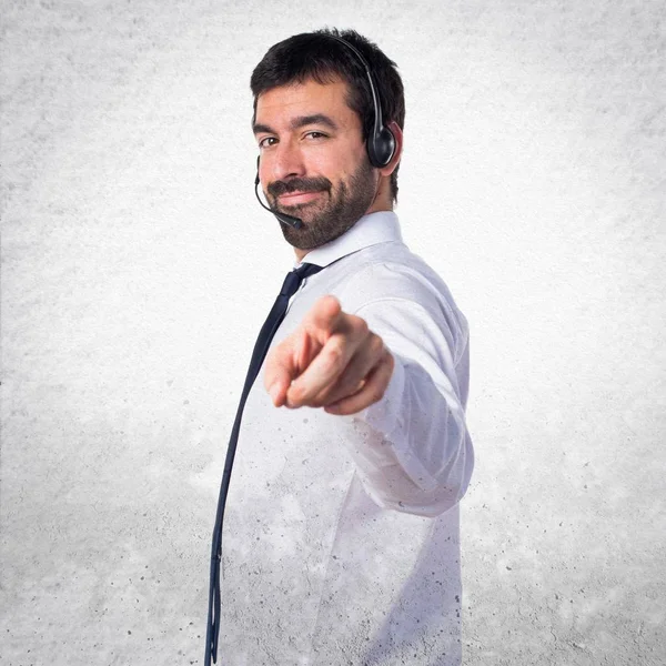 Joven con un auricular apuntando al frente en el respaldo texturizado — Foto de Stock