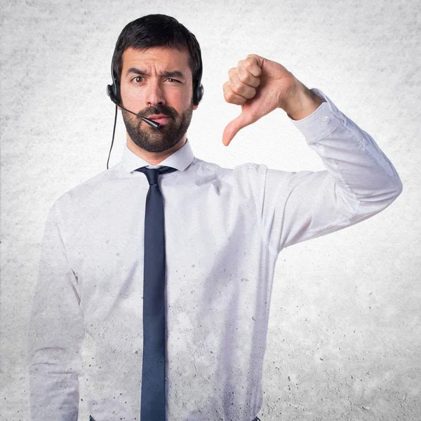 Young man with a headset doing bad signal on textured background — Stock Photo, Image