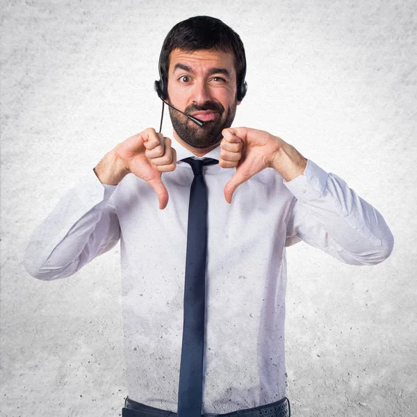 Joven con un auricular haciendo mala señal sobre fondo texturizado — Foto de Stock