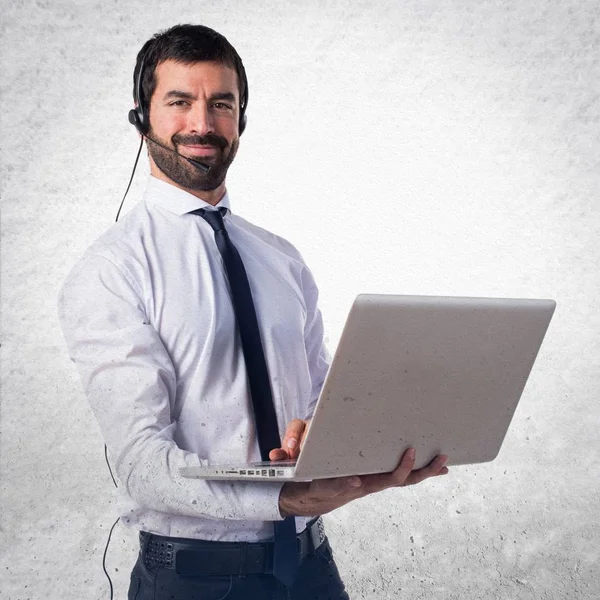 Yakışıklı telemarketer adam ile dokulu arka plan üstünde laptop — Stok fotoğraf