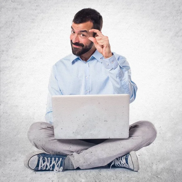 Homem com laptop fazendo sinal minúsculo no fundo texturizado — Fotografia de Stock