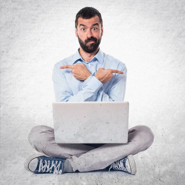Homem com laptop apontando para as laterais com dúvidas sobre textur — Fotografia de Stock