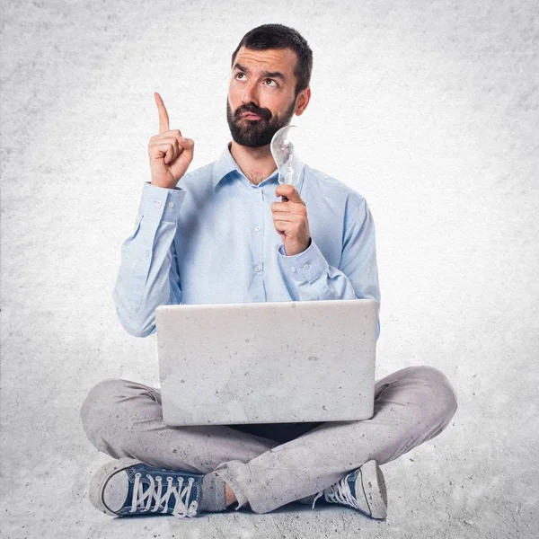 Homem com laptop segurando uma lâmpada no fundo texturizado — Fotografia de Stock