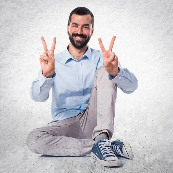 Pohledný muž dělá gesto vítězství na podklad s texturou — Stock fotografie