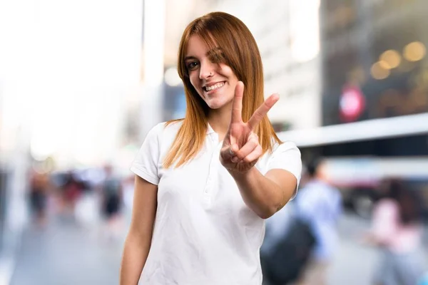 Schönes junges Mädchen macht Siegesgeste auf unkonzentriertem Hintergrund — Stockfoto