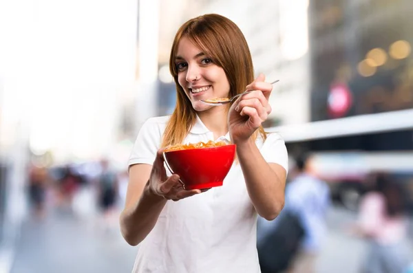 Joyeux Belle jeune fille mangeant des céréales à partir d'un bol sur fond flou — Photo