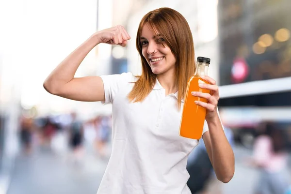 Menina bonita feliz segurando um suco de laranja em fundo desfocado — Fotografia de Stock