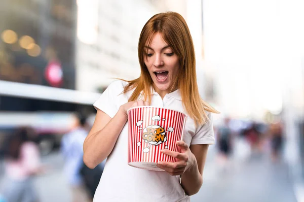 Surprised Beautiful young girl eating popcorns on unfocused back — Stock Photo, Image
