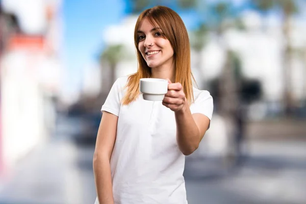 Happy Beautiful menina segurando uma xícara de café em fundo desfocado — Fotografia de Stock