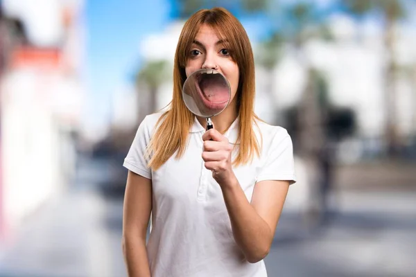 Hermosa joven con lupa sobre fondo desenfocado —  Fotos de Stock