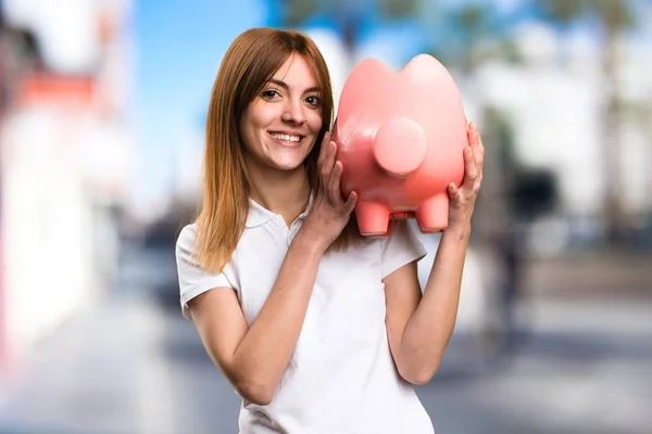 Glücklich schönes junges Mädchen hält ein Sparschwein auf unkonzentriertem Hintergrund — Stockfoto