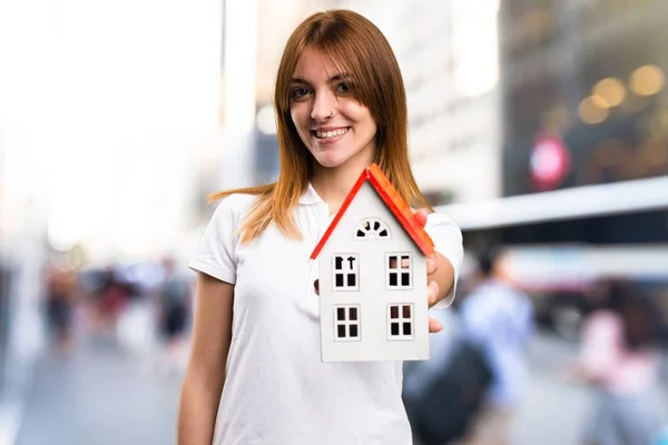 Счастливая молодая девушка, держащая маленький домик на расфокусированном фоне — стоковое фото