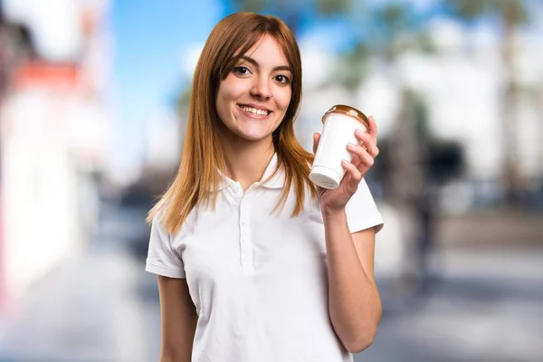 Joyeux Belle jeune fille tenant une tasse de café sur fond flou — Photo