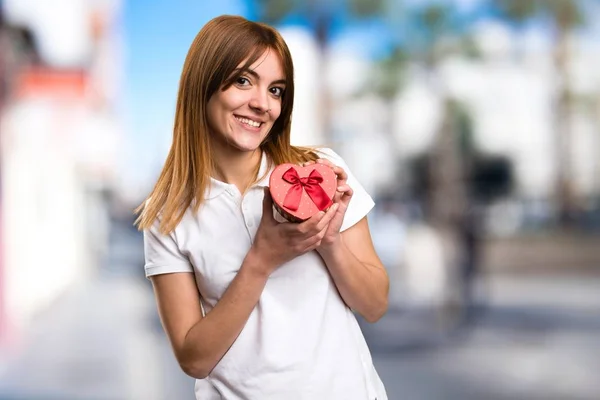 Happy Beautiful young girl holding a gift on unfocused background — Stock Photo, Image