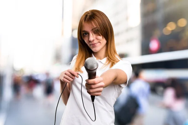 Belle jeune fille chantant avec microphone sur fond flou — Photo