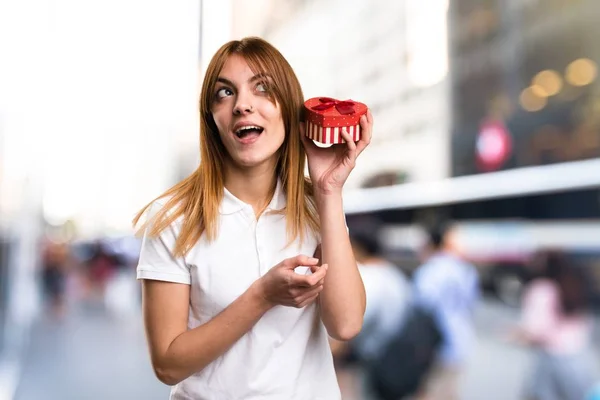 Vacker ung flicka som håller en gåva på ofokuserat bakgrund — Stockfoto