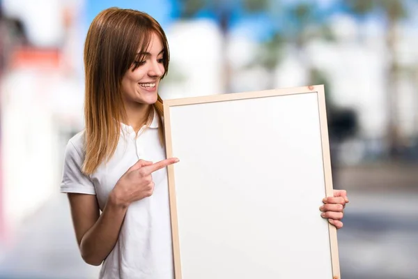 Glücklich schönes junges Mädchen mit einem leeren Plakat auf unkonzentriertem Hintergrund — Stockfoto