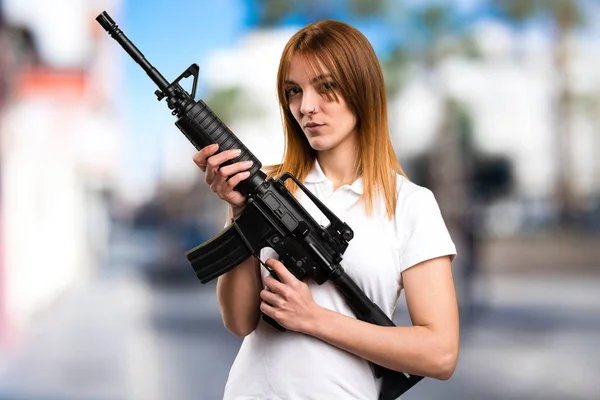 Schönes junges Mädchen mit einem Gewehr auf unkonzentriertem Hintergrund — Stockfoto