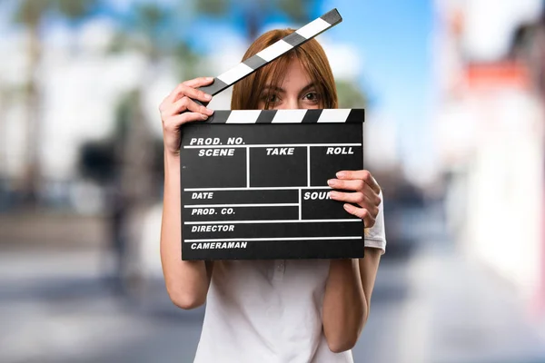 Beautiful young girl holding a clapperboard on unfocused backgro — Stock Photo, Image