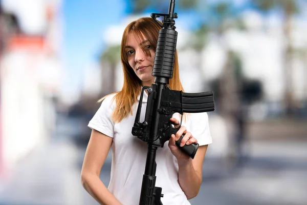 Beautiful young girl holding a rifle on unfocused background — Stock Photo, Image