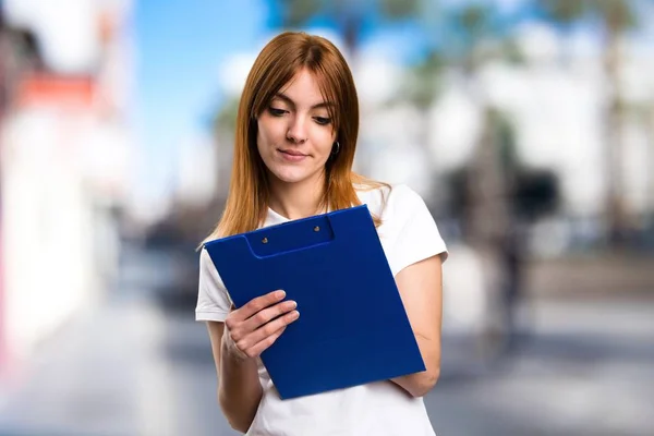 Beautiful young girl holding a folder on unfocused background — Stock Photo, Image