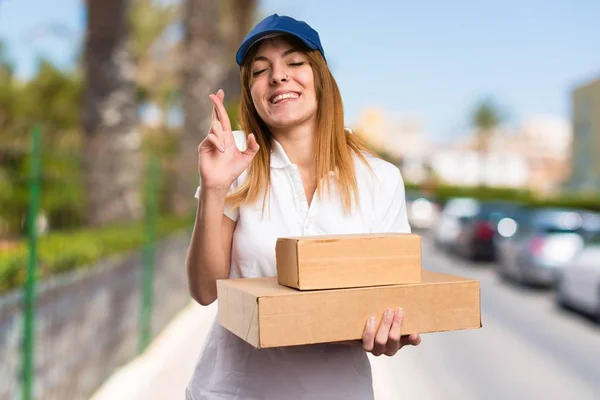 Delivery woman with her fingers crossing on unfocused background