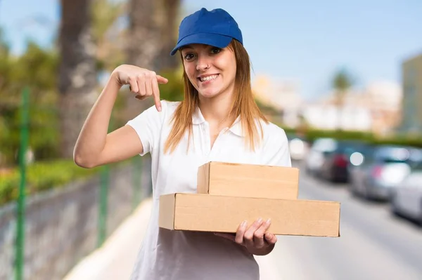 Delivery woman pointing down on unfocused background — Stock Photo, Image