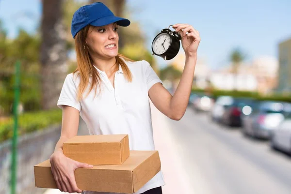 Surprised Delivery woman holding vintage clock on unfocused background — Stock Photo, Image