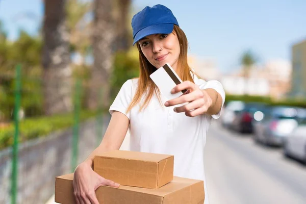 Mulher de entrega segurando um cartão de crédito em fundo desfocado — Fotografia de Stock