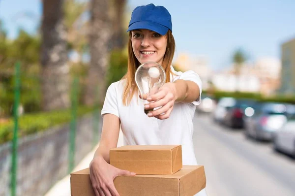 Delivery woman holding a bulb on unfocused background