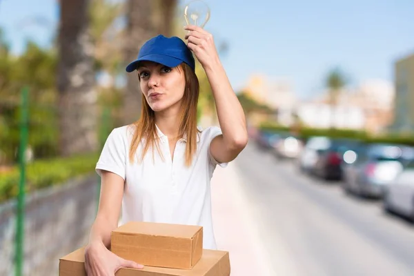 Delivery woman holding a bulb on unfocused background