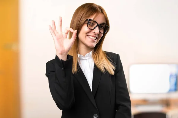 Joven mujer de negocios haciendo OK signo en la oficina sobre fondo desenfocado —  Fotos de Stock