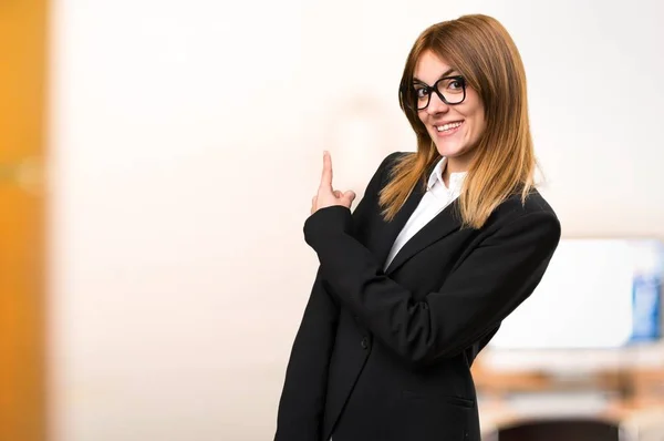 Ung affärskvinna som pekar tillbaka på kontoret på ofokuserat bakgrund — Stockfoto