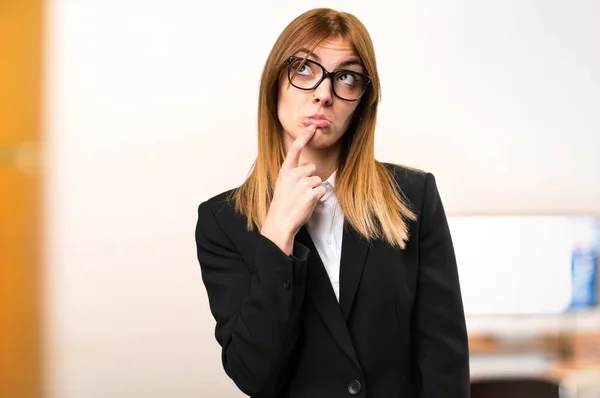 Joven mujer de negocios que tiene dudas en la oficina sobre fondo desenfocado — Foto de Stock