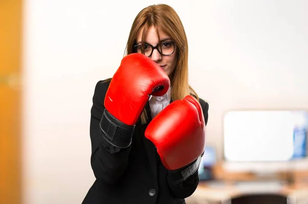 Junge Geschäftsfrau mit Boxhandschuhen im Büro vor unkonzentriertem Hintergrund — Stockfoto