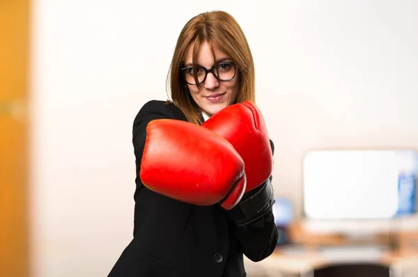 Genç iş kadını odaklanmamış arka plan üzerinde ofiste boks eldivenli — Stok fotoğraf