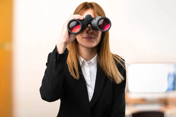 Joven mujer de negocios con prismáticos en la oficina sobre fondo desenfocado —  Fotos de Stock