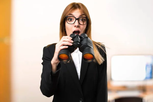 Young business woman with binoculars in the office on unfocused background — Stock Photo, Image