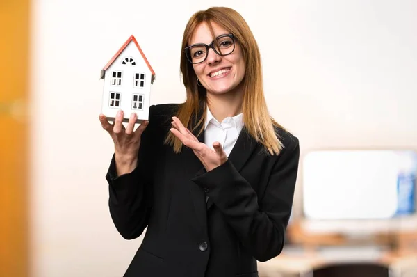 Молодая деловая женщина держит маленький дом в офисе на нецеленаправленном фоне — стоковое фото